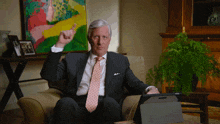 a man in a suit and tie is sitting in a chair and pointing up