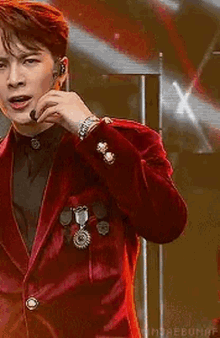 a young man wearing a red suit and a microphone on his head is standing on a stage .