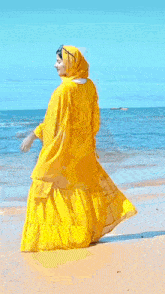 a woman in a long yellow dress is walking on the beach