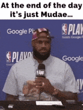 a man holding a microphone with the words at the end of the day it 's just mudae on the bottom