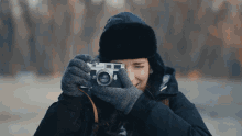 a woman wearing gloves and a black hat is taking a picture with a camera