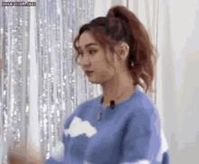 a woman in a blue sweater with clouds on it is standing in front of a white curtain .
