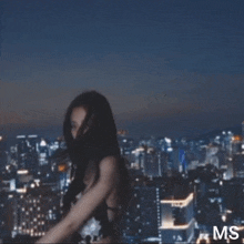 a woman in a black strapless dress is standing in front of a city skyline at night .