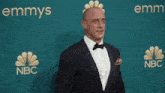 a man in a tuxedo is standing next to a woman in a black dress in front of an emmys sign