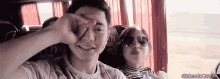 a man and a woman are sitting on a bus and making a peace sign .