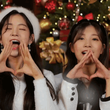 two girls making a heart with their hands in front of a christmas tree
