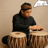 a man in a black shirt is playing drums with a cat behind him