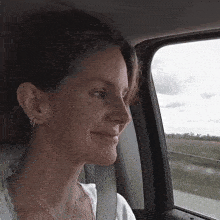 a woman wearing hoop earrings is smiling while looking out a car window