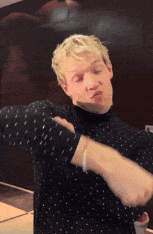 a man with blonde hair is wearing a black polka dot shirt and making a funny face