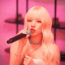 a woman singing into a microphone with a pink background