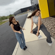 two women are dancing on a sidewalk in front of a building with the letter o on it