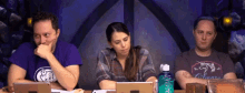 a group of people are sitting at a table with laptops and a bottle of water .