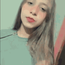 a young woman with long hair and red lipstick is wearing a blue shirt and looking at the camera .