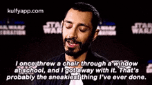 a man with a beard is sitting in front of a star wars sign and talking .