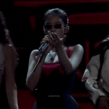 a woman wearing sunglasses and a red tank top is holding a microphone while dancing on a stage .