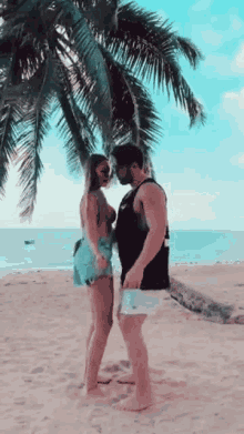 a man and woman are standing on a beach under a palm tree