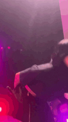 a man in a black shirt is dancing on a stage with purple lights behind him
