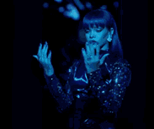 a woman with blue hair is standing in a dark room with her hands outstretched
