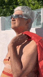 an older woman wearing sunglasses holds a red towel over her shoulders