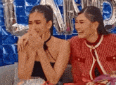 two women are sitting next to each other on a couch laughing and crying .