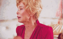 a woman in a red dress is sitting on a bed and looking at the camera .