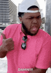 a man wearing a pink shirt and a white hat is giving a thumbs up and says damn !!!
