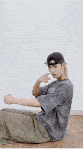 a man wearing a hat and glasses is sitting on the floor with his arms outstretched