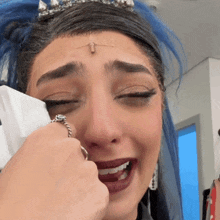 a woman with blue hair is crying while wearing a tiara