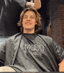 a man is getting his hair cut by a man in a mood studio cape