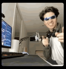a man wearing sunglasses is holding a video game controller in front of a computer .