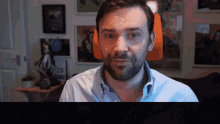 a man with a beard looks at the camera in front of a wall with pictures on it