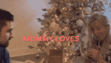 a man and a woman are sitting in front of a christmas tree with the words " mommy loves " on the bottom