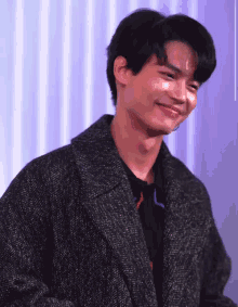 a young man wearing a black coat is smiling .