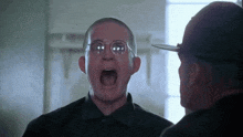 a man wearing glasses is screaming at another man in a black shirt .