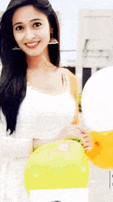 a woman in a white dress is holding a yellow balloon and smiling