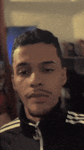 a young man with a beard and mustache wearing a black adidas jacket