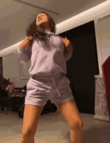 a woman in a purple shirt and shorts is dancing in a living room