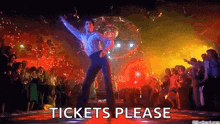 a man is dancing in front of a crowd at a disco and the words `` tickets please '' are visible .