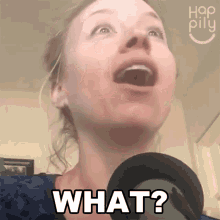 a woman singing into a microphone with her mouth open and the words what written on her face