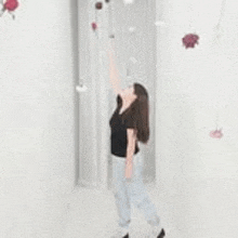 a woman is standing in front of a white wall with flowers hanging from it .