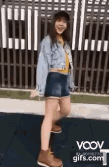 a girl in a denim jacket and shorts is dancing on the sidewalk .