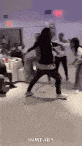 a group of people are dancing in a room with tables and chairs .