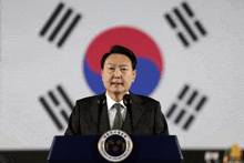 a man stands at a podium in front of a flag