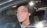a woman wearing glasses is driving a car and looking out the window