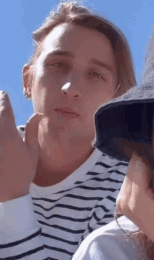 a man in a striped shirt and a woman in a hat are sitting next to each other in front of a blue sky .