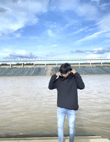 a man wearing a black hoodie is standing in front of a body of water
