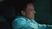 a man in a blue shirt is smiling while driving