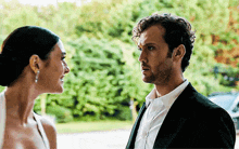 a man and a woman are looking at each other with trees in the background