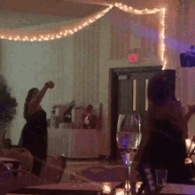 a woman in a black dress is dancing in a room with a red exit sign in the background