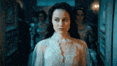 a woman in a white lace dress stands in a dark room